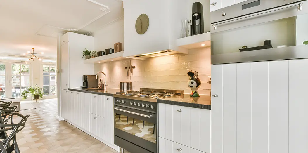 Cocina  amplia con todos los muebles situados a lo largo de una pared con muebles blancos y encimera de color negro incluye fuegos de gas y horno en el mismo aparato